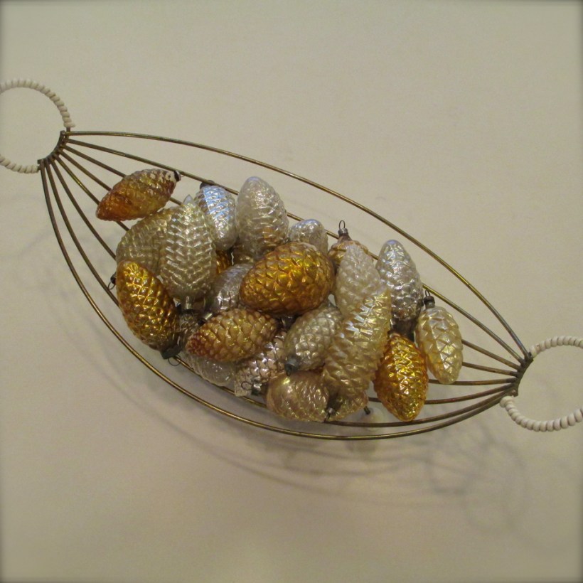 A 1950's fruit bowl filled with old glass pinecone ornaments in silvers and golds.